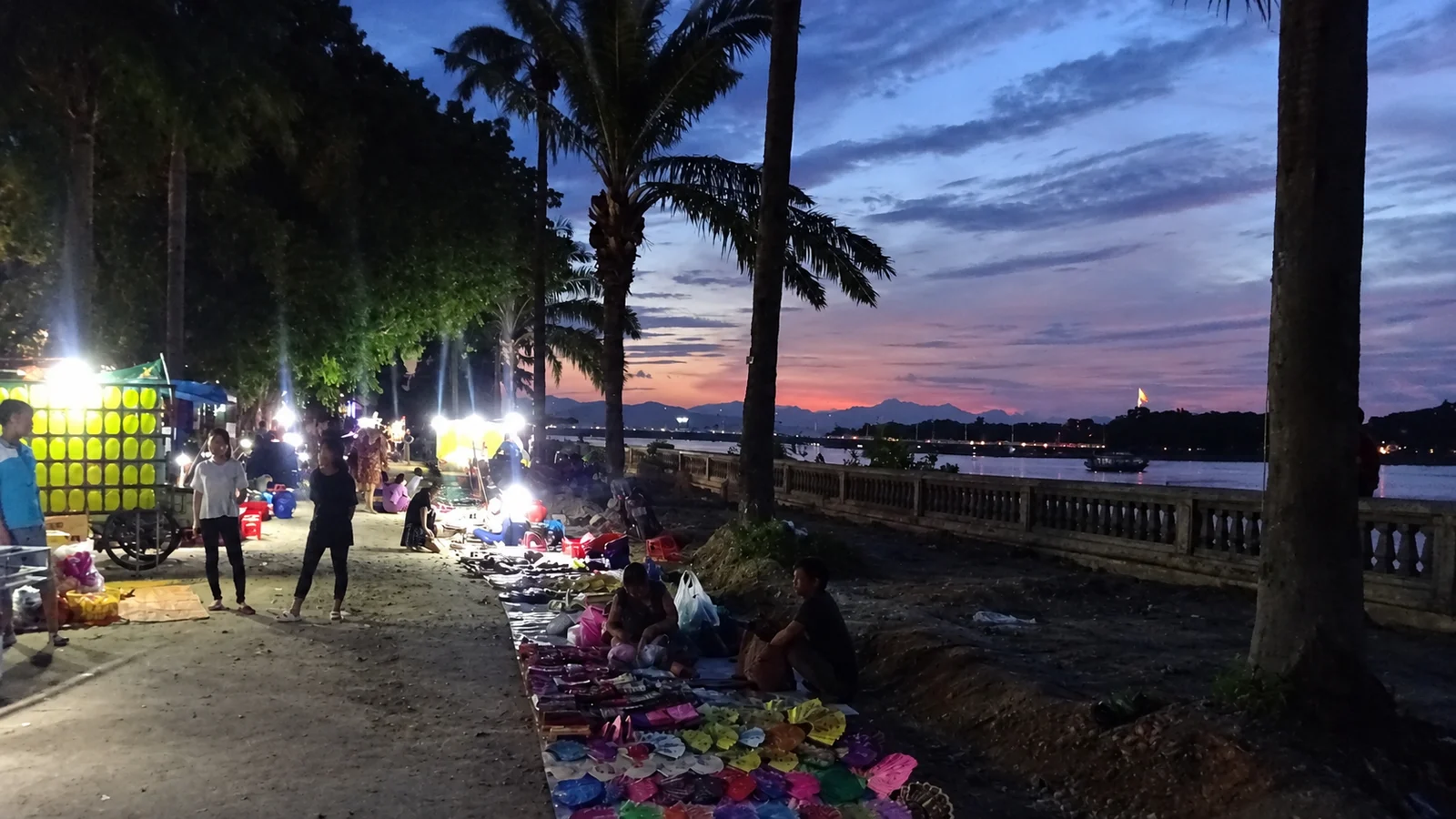 Market stalls and people along the riverside in Huế at dusk