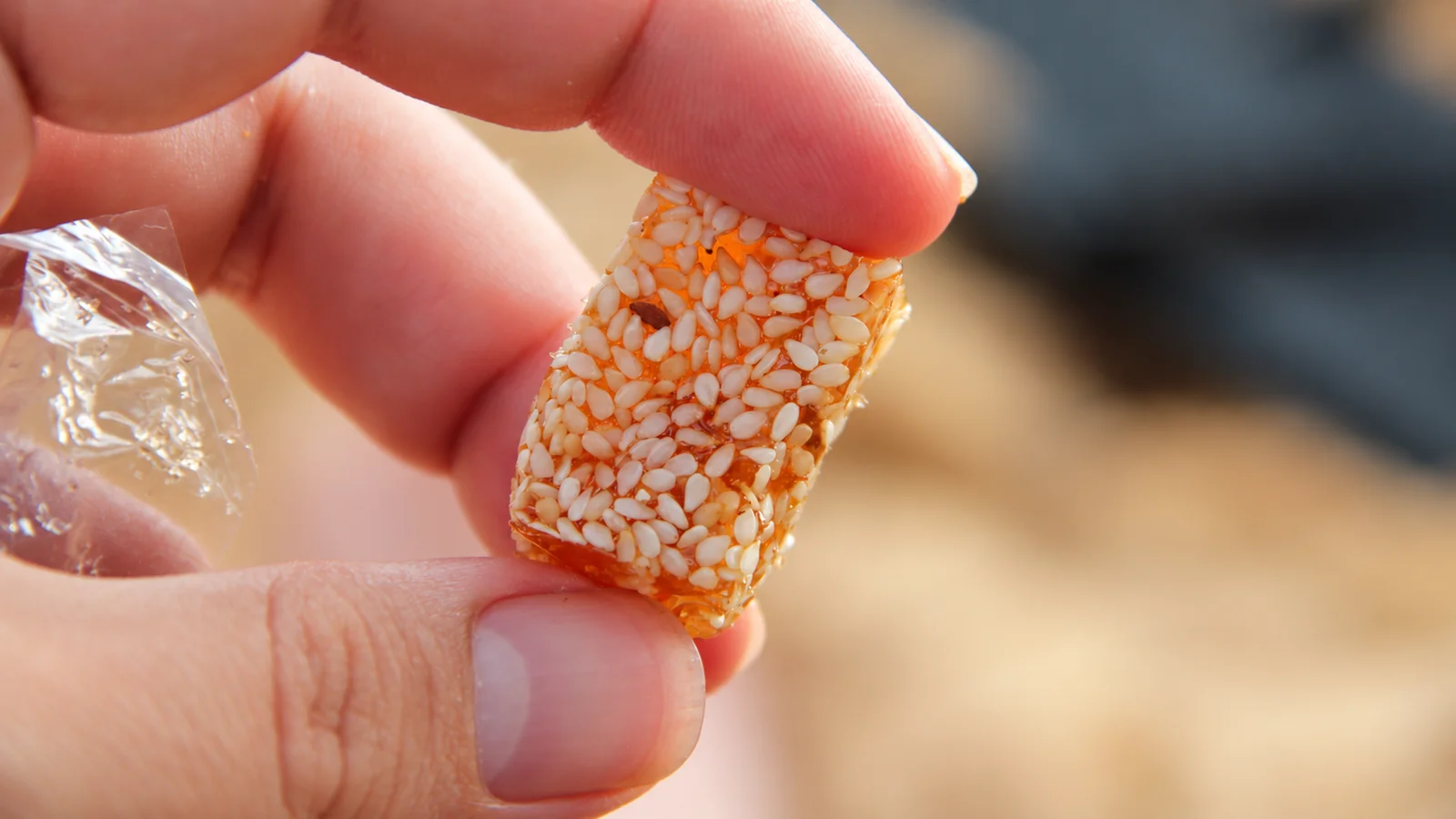 A sesame-coated piece of mè xửng candy held between two fingers